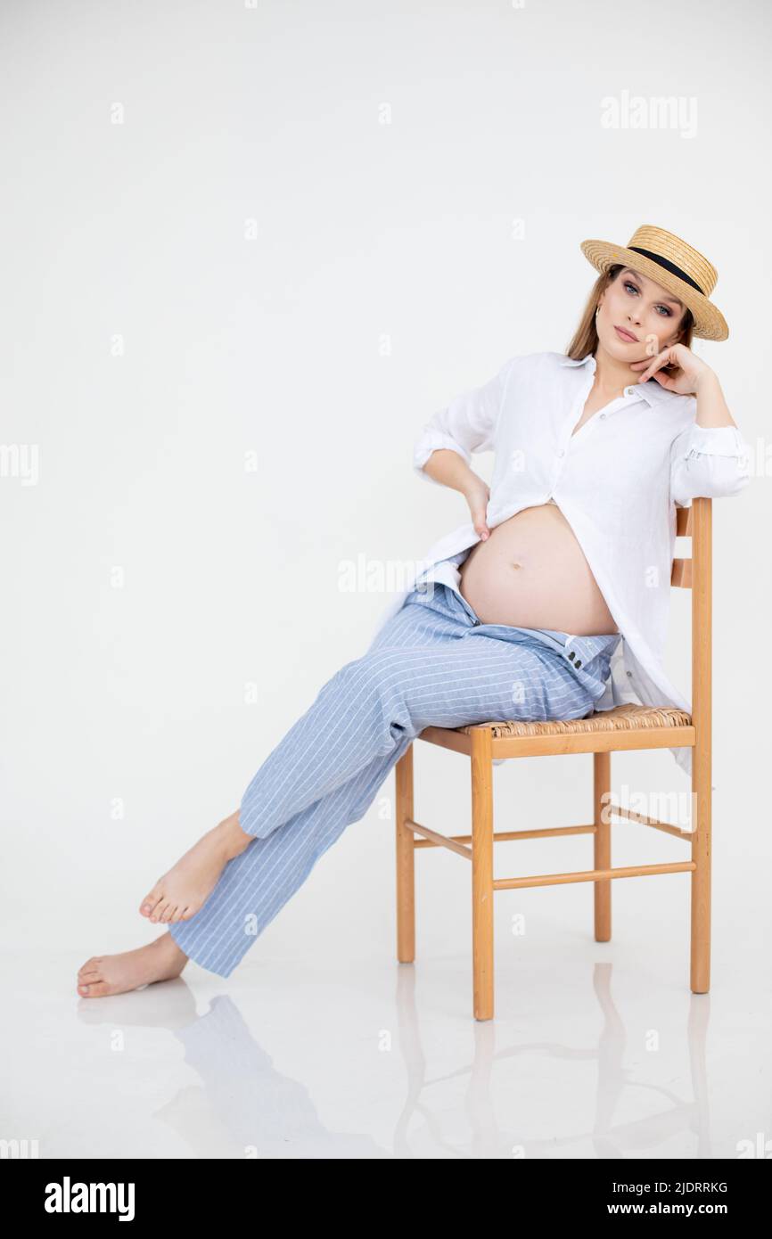 Pregnant woman in linen clothes on white background sitting on chair. Pregnancy, maternity