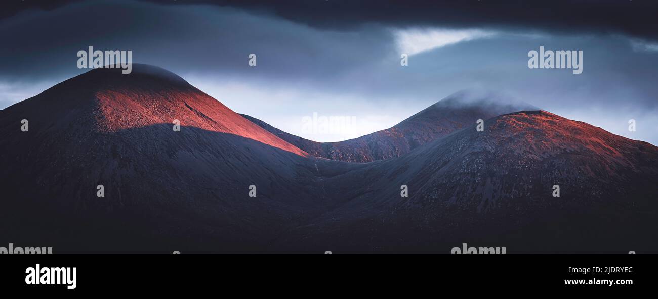 Beautiful morning on Isle of Skye, Scotland.Cloudy sky over mountains with slopes lit by first sunlight.Panoramic landscape scenery. Stock Photo