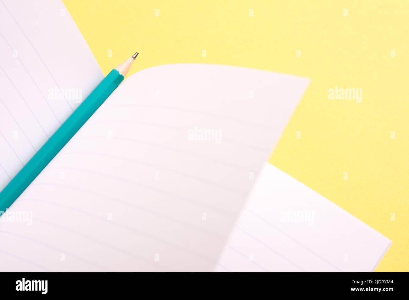 Aqua blue pencil and an open notebook on yellow background. Stock Photo