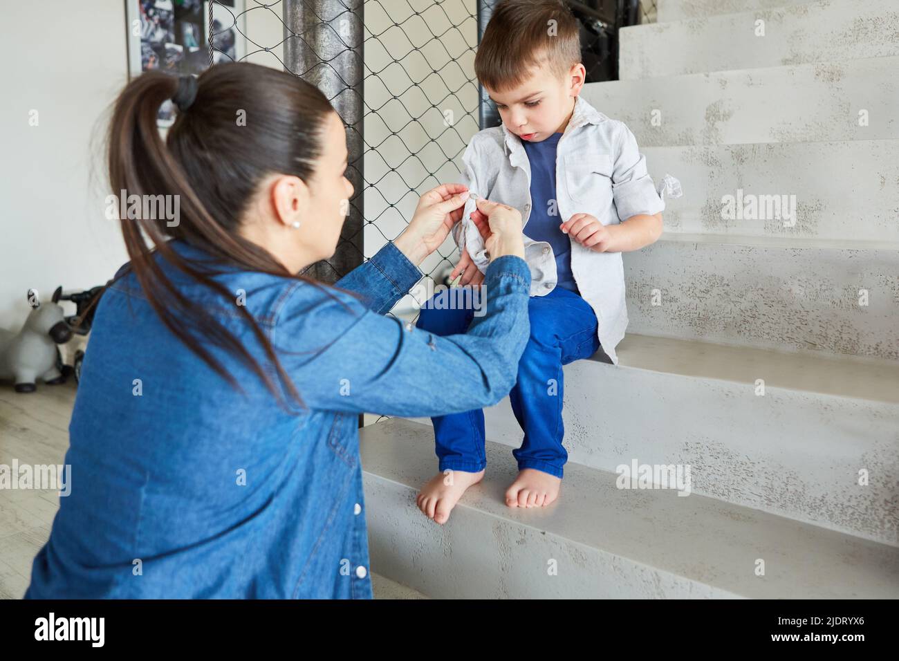 Single mother helping her son put on a shirt at home Stock Photo
