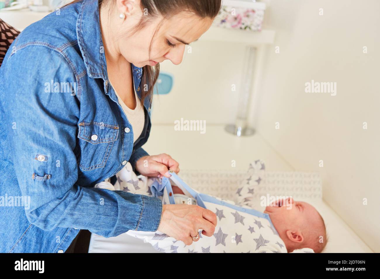 Caring mother changing diaper at her baby on changing table at home Stock Photo