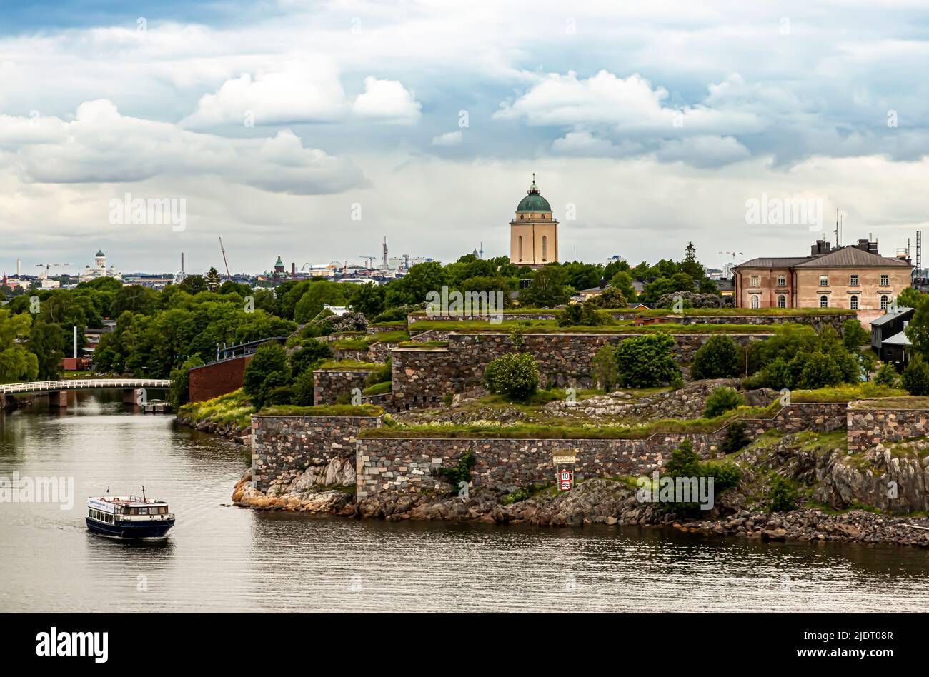 View of the Suomenlinna sea fortress. A ferry in the foreground. Downtown Helsinki in the background. Stock Photo