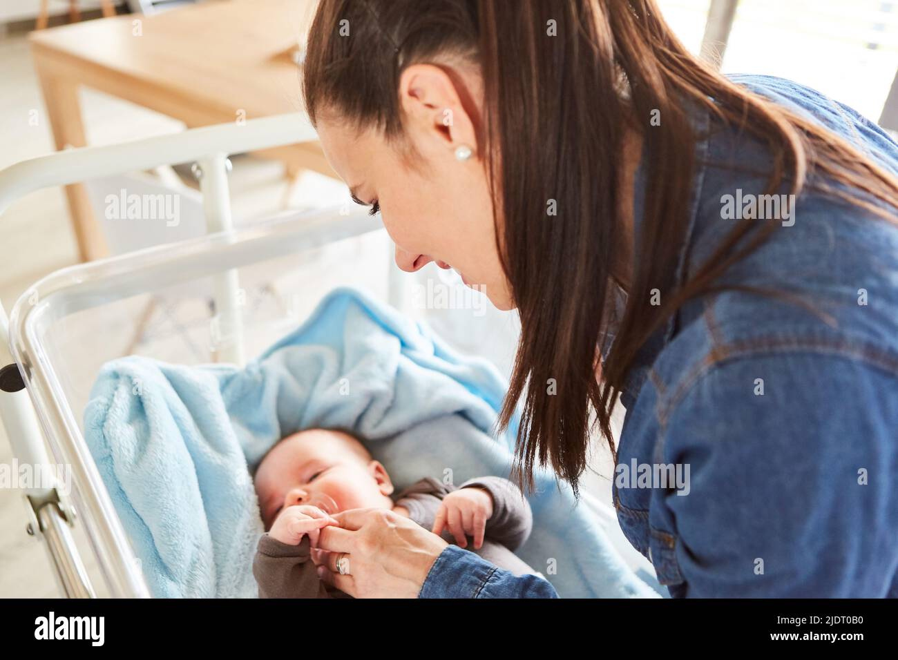 Mother lovingly takes care of her baby while falling asleep in the cot