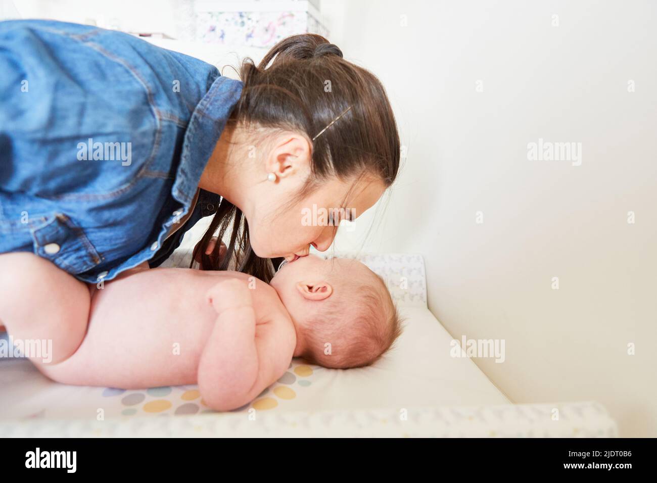 Mother gives her baby a tender kiss for motherly love on the changing table Stock Photo