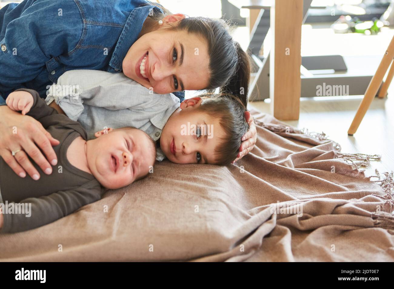 Happy mother cuddling with son and newborn baby on sofa in living room Stock Photo
