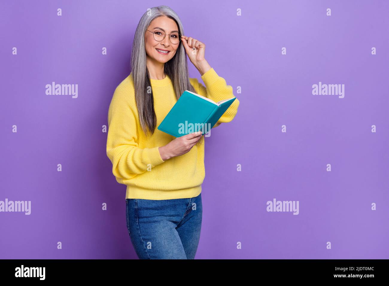 Photo of beautiful mature college teacher reading book novel to her students isolated on violet color background Stock Photo