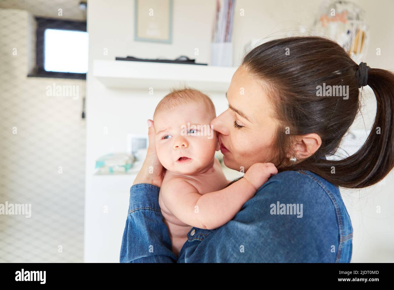 Mother gives her baby a tender kiss on the cheek for affection and motherly love Stock Photo