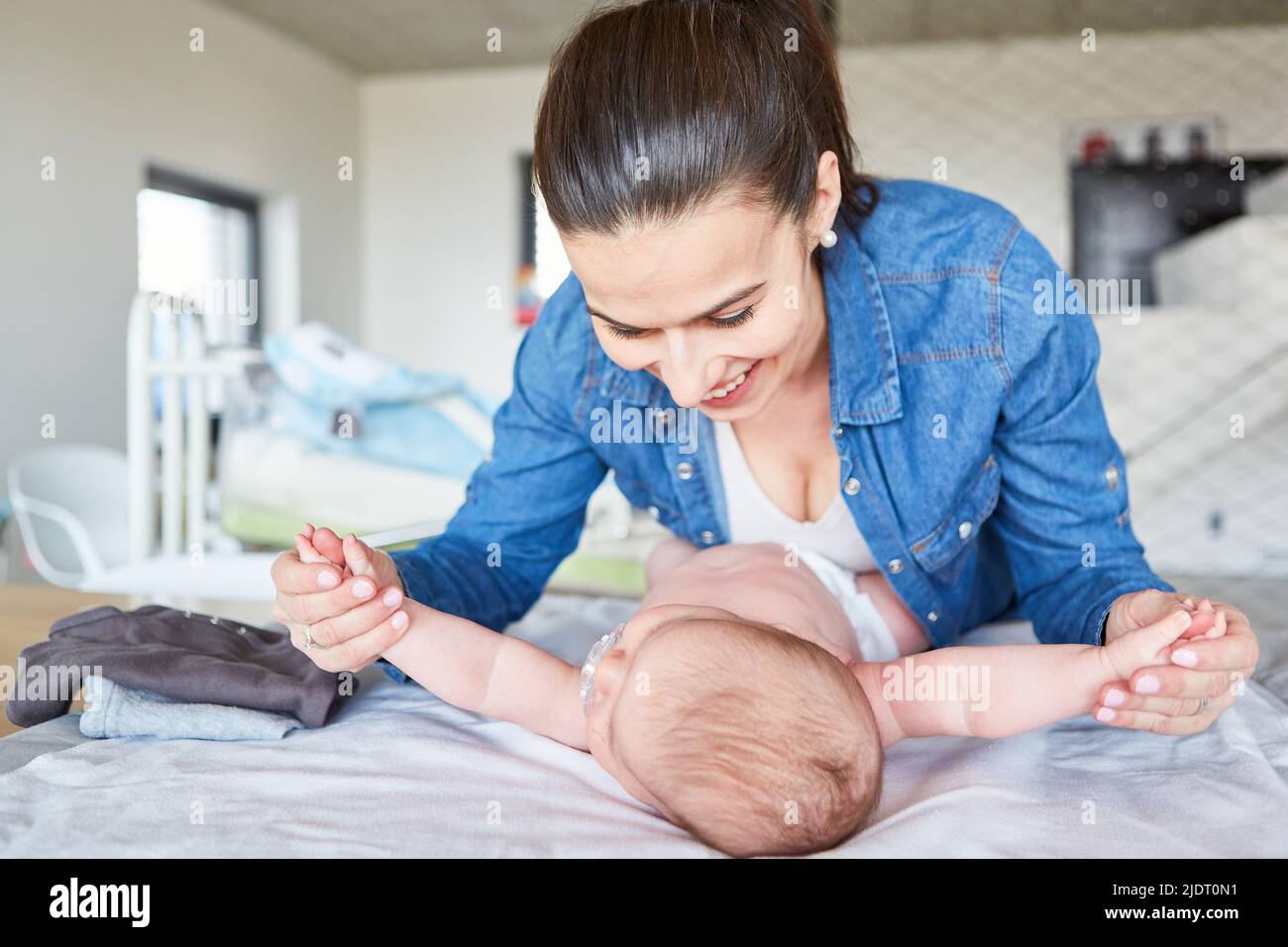 Mother holds her newborn baby by hands while changing diaper on the changing table Stock Photo