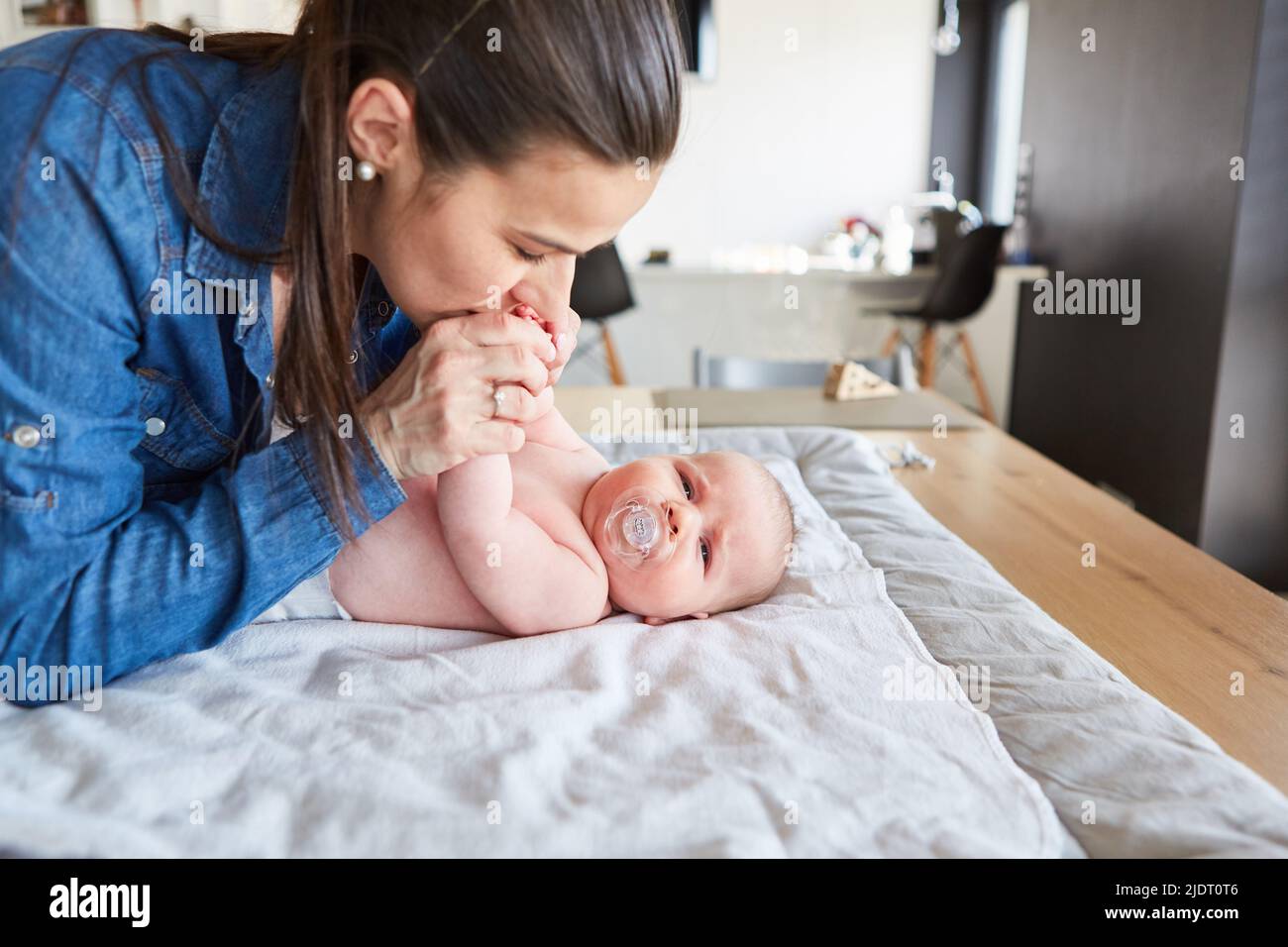 Loving mother gives her baby a kiss while changing diaper on the changing table Stock Photo