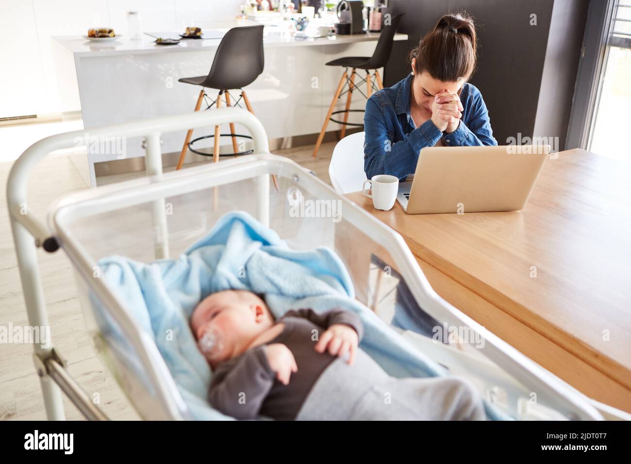 Exhausted single mother in home office with sleeping baby in foreground Stock Photo