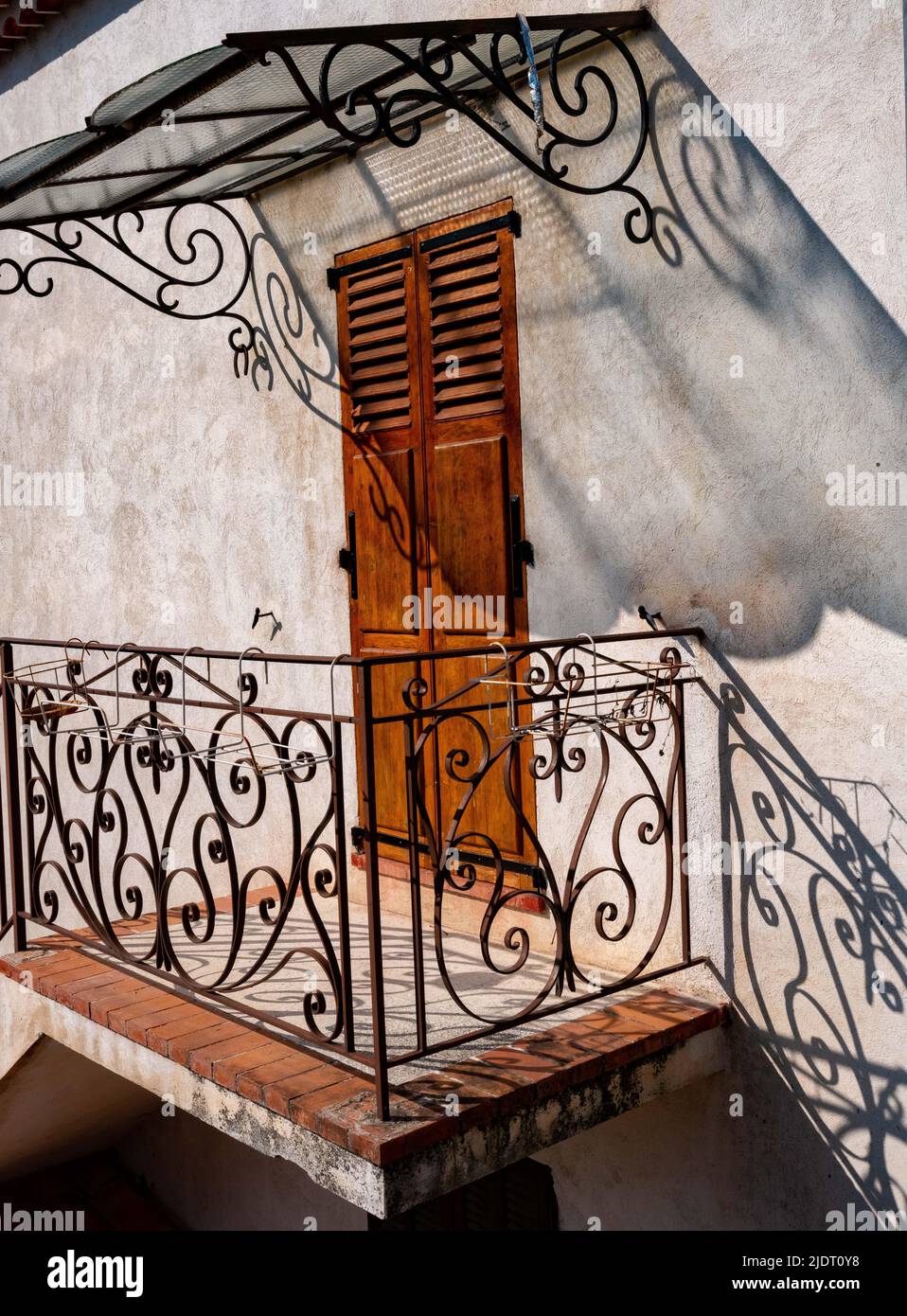 The sun casts many shadows of a wrought iron awning and fence in a doorway of a Provencal house in the village of Villars sur Var in the lower Alps Stock Photo