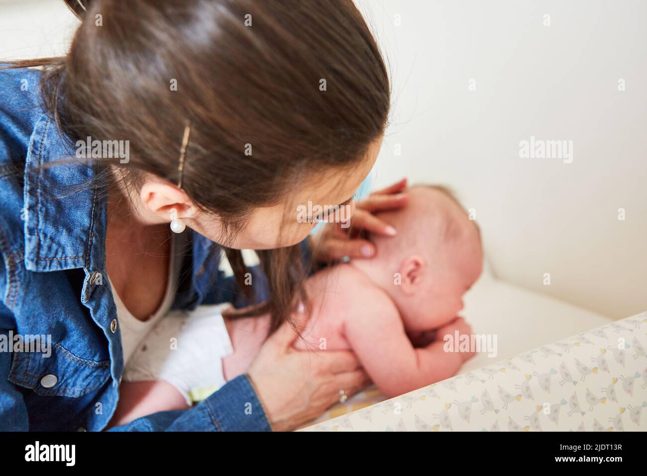 Caring mother carefully examines her baby's delicate skin while changing diaper Stock Photo