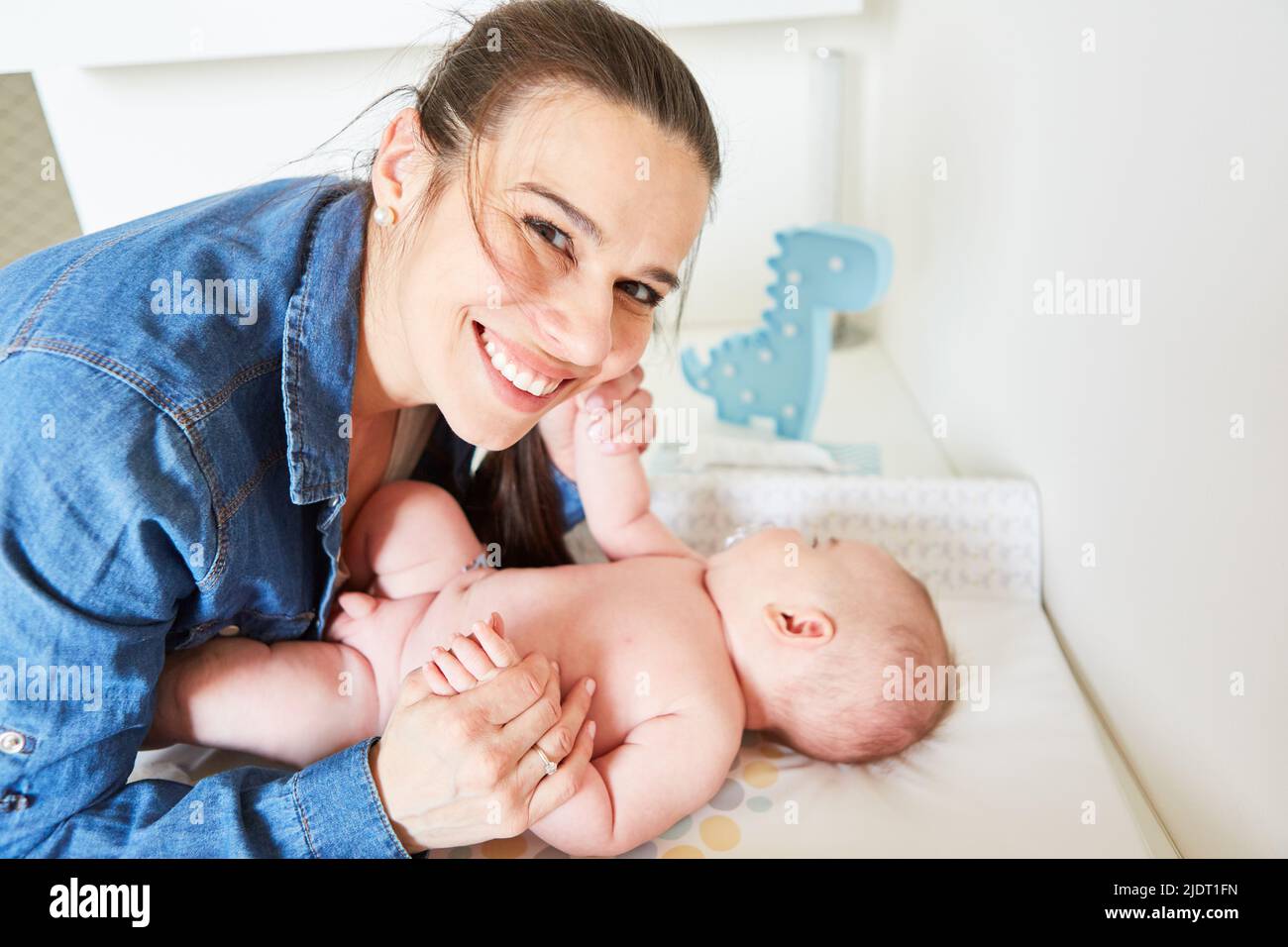 Happy mother lovingly holds her baby by the hands while caring for it on the changing table Stock Photo