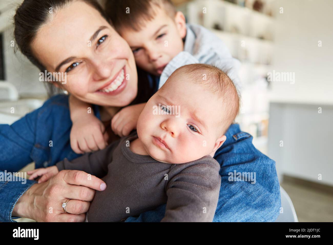 Happy smiling mother with baby and big brother cuddling together at home Stock Photo