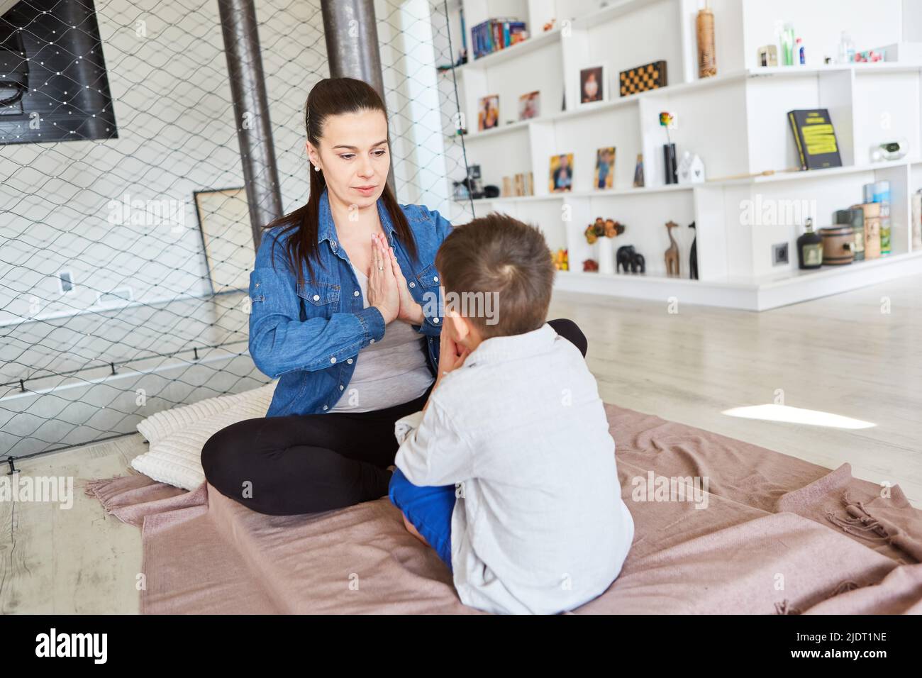 Mother sits across from her son doing a yoga exercise at home in the living room Stock Photo