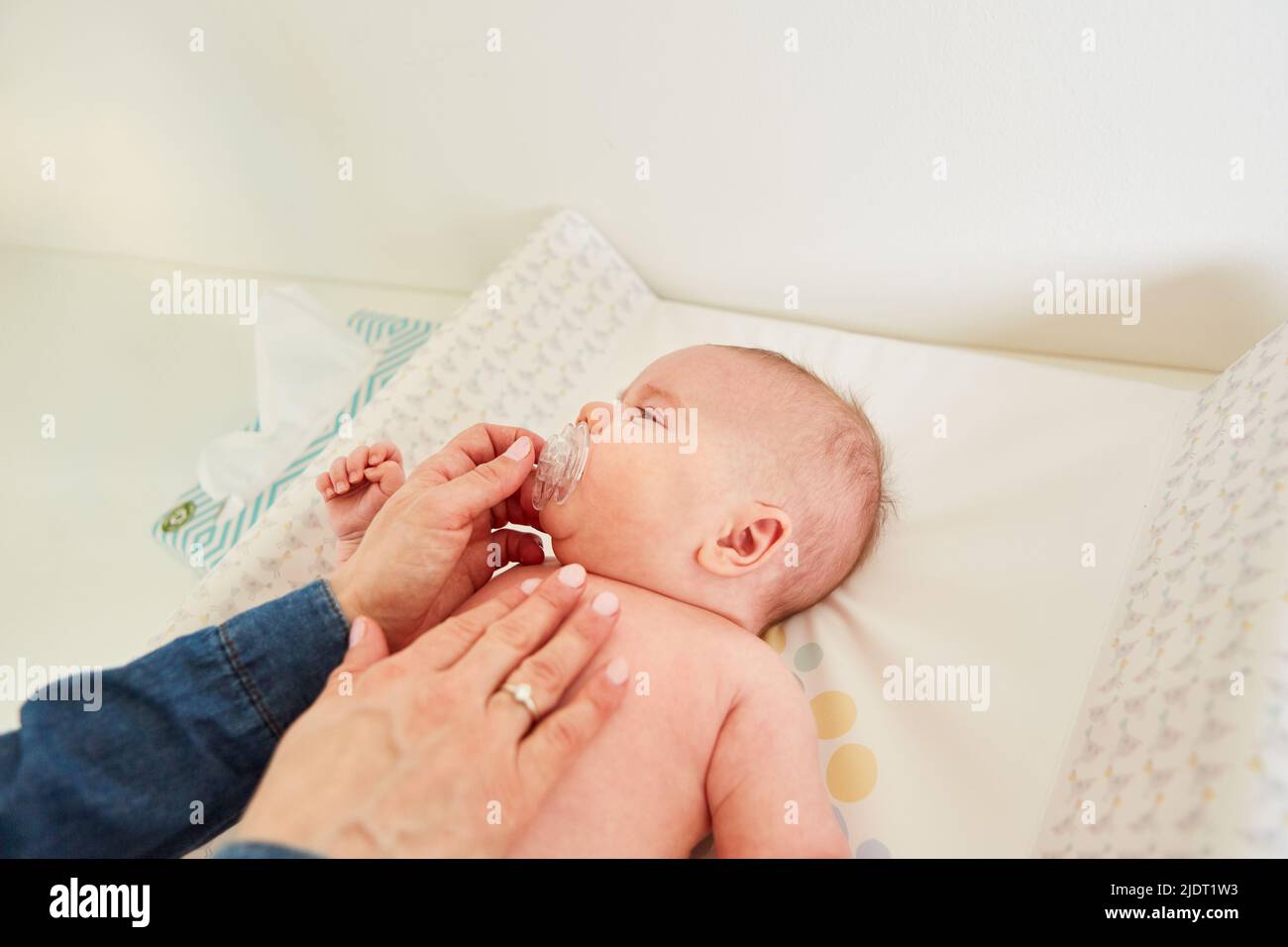 Caring mother gives her baby a pacifier for comfort on the changing table Stock Photo