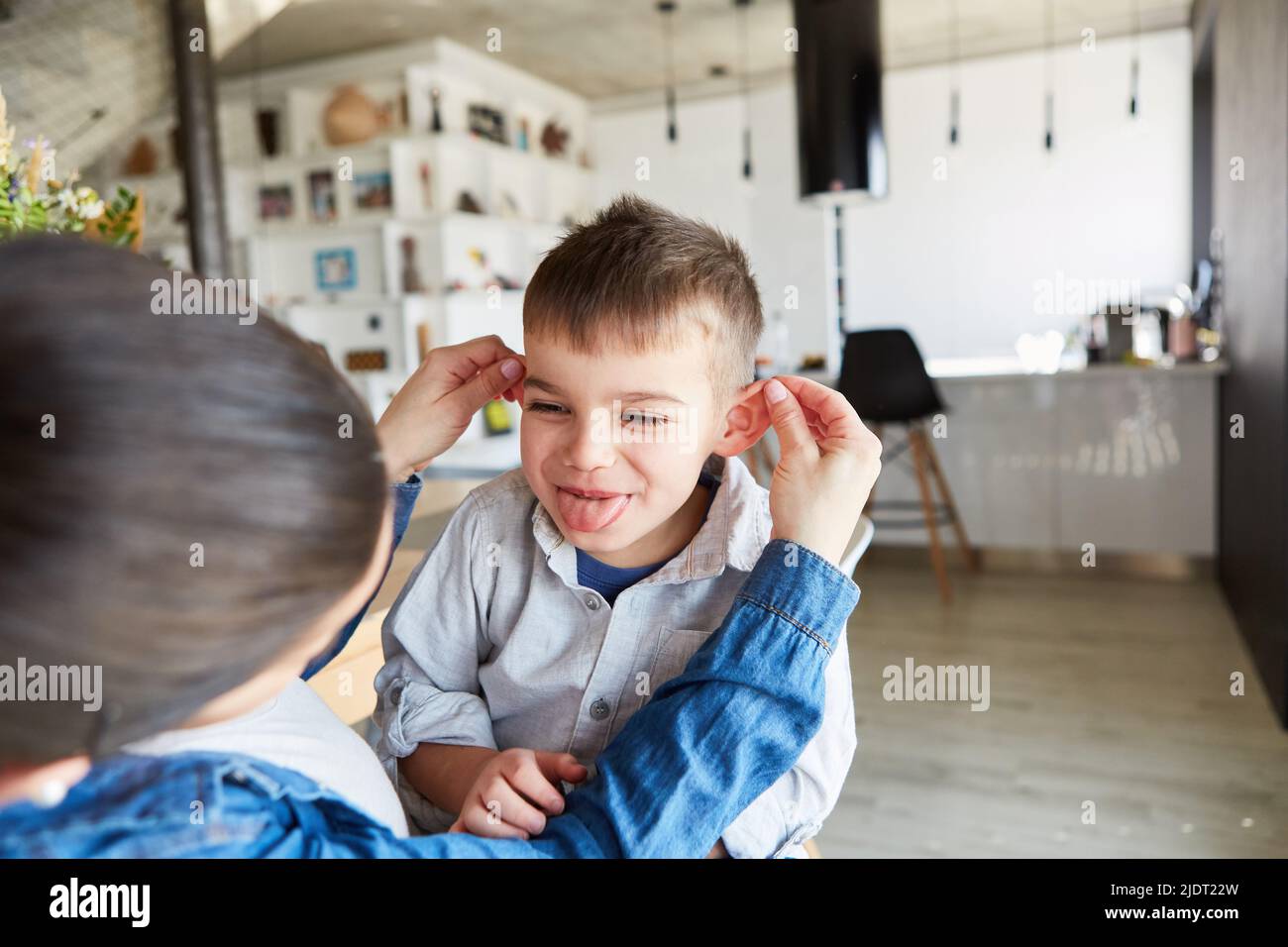 Mother pulls the ears of her rascal son and he cheekily sticks out his tongue Stock Photo