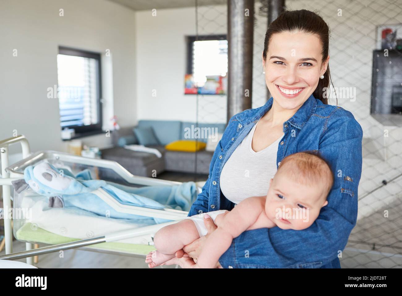 Happy smiling mother holding newborn baby in her arms in front of cot at home Stock Photo