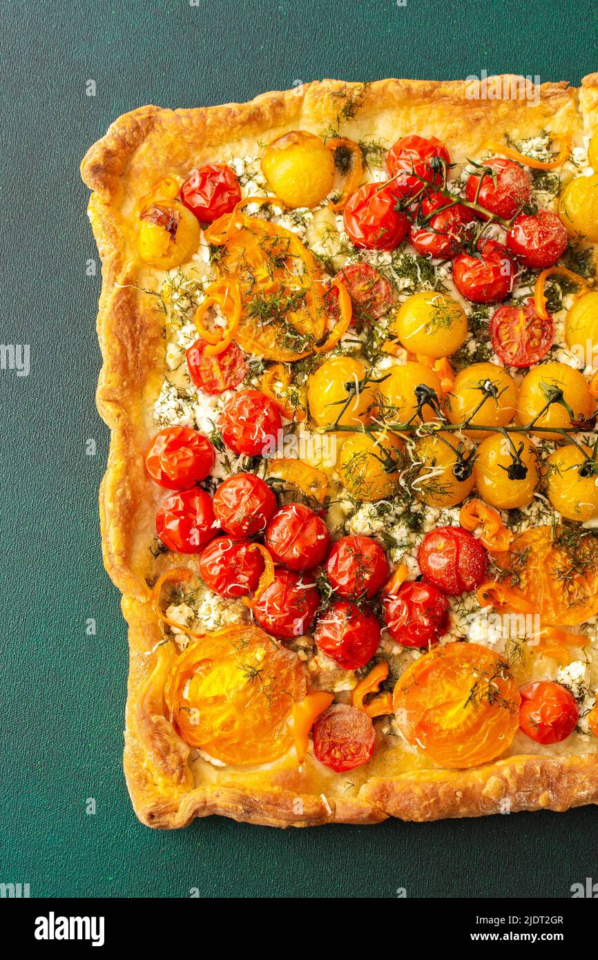 Homemade pie made of puff pastry and yellow, orange and red tomatoes, savory square pie on a green background, top view, copy space Stock Photo