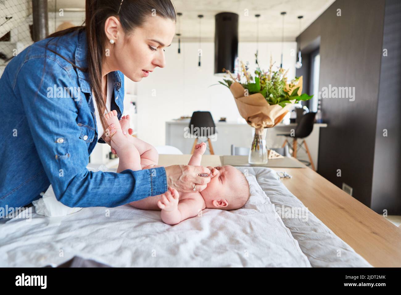 Caring mother gives her baby a pacifier for comfort while changing diaper Stock Photo