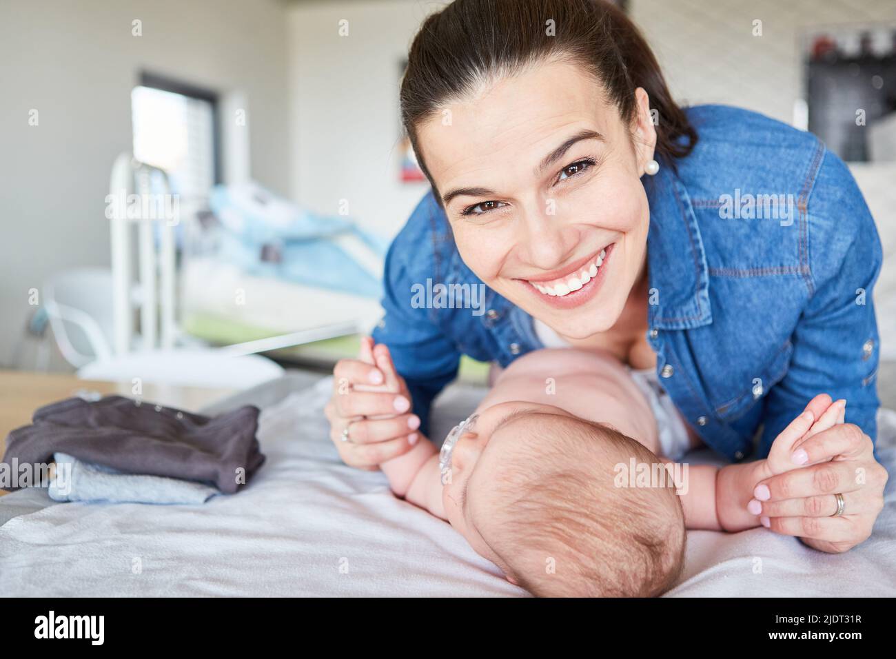 Happy smiling mother holding baby on changing table for maternity and motherly love Stock Photo