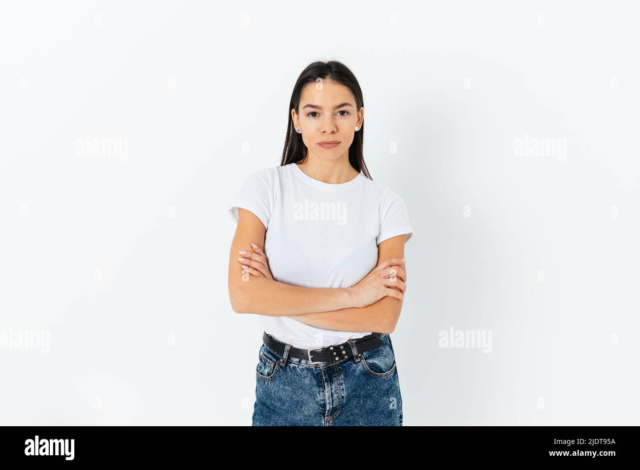 Portrait of calm confident young beautiful brunette woman wearing white t-shirt and blue jeans looking at camera on white studio background Stock Photo