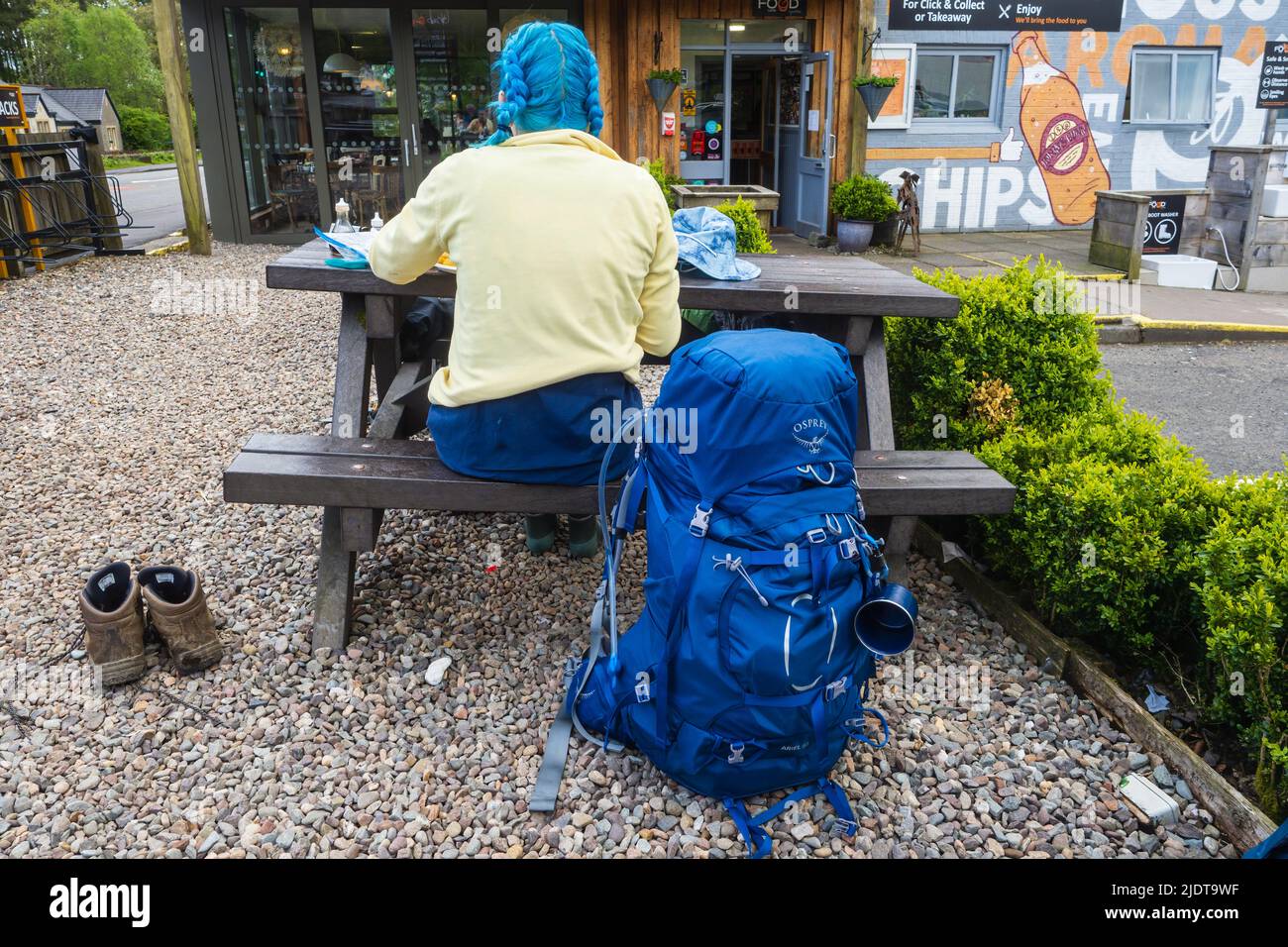 19.05.2022 Tyndrum, Argyll, Scotland, UK. Female hiker wearing yellow with blue backpack resting at the fish and chips stopover in Tyndrum on the West Stock Photo