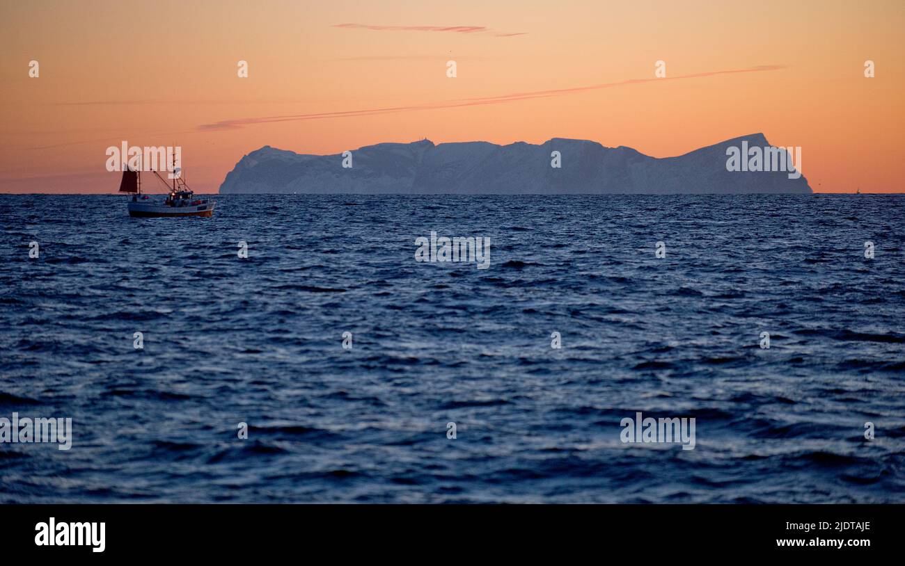 Small fishingboat at sunrize in the sea off Vaeröy (Lofoten, Nordland) seen in the background. Stock Photo