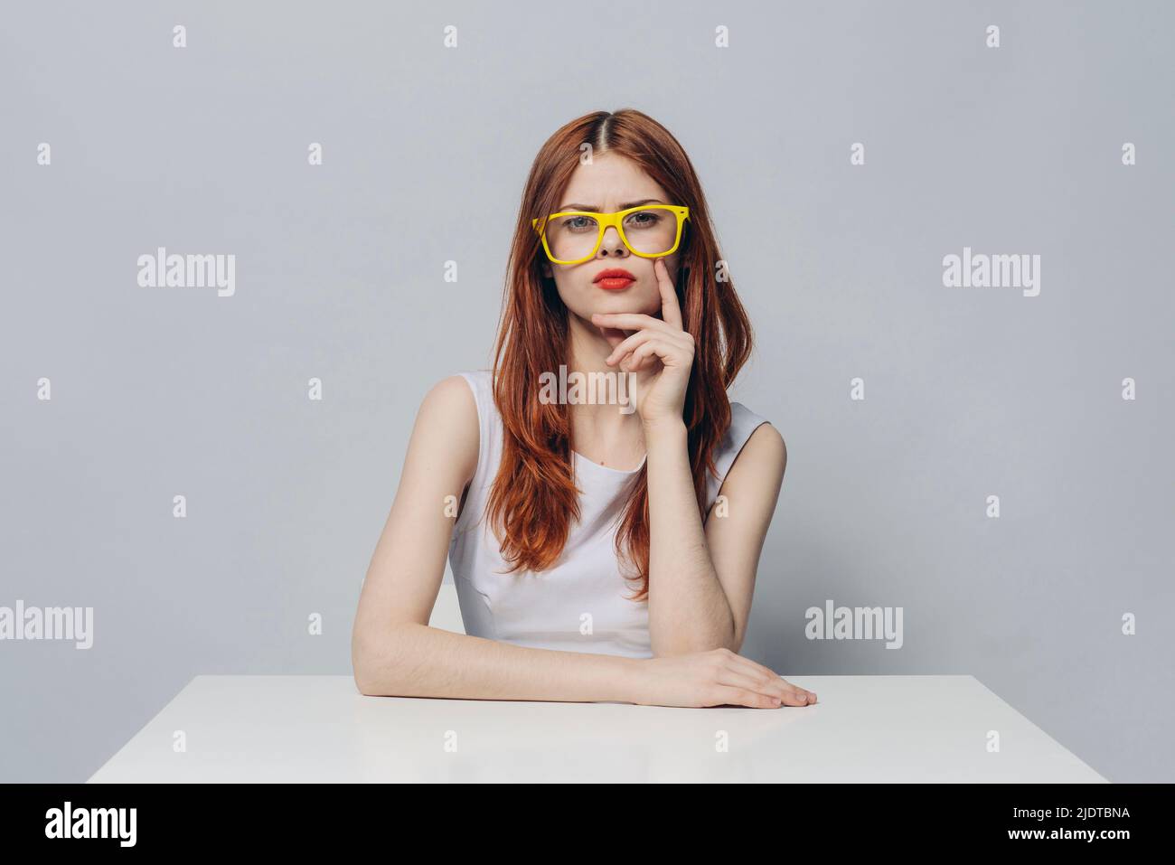 Serious Caucasian woman sitting at table wearing yellow eyeglasses Stock Photo