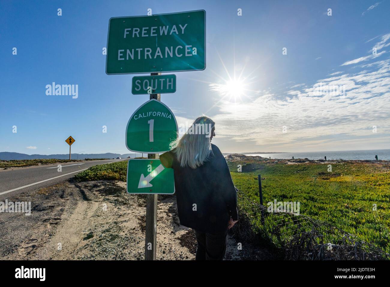 USA, California, Carmel, Rear view of senior blonde woman at Highway 1 entrance sign Stock Photo