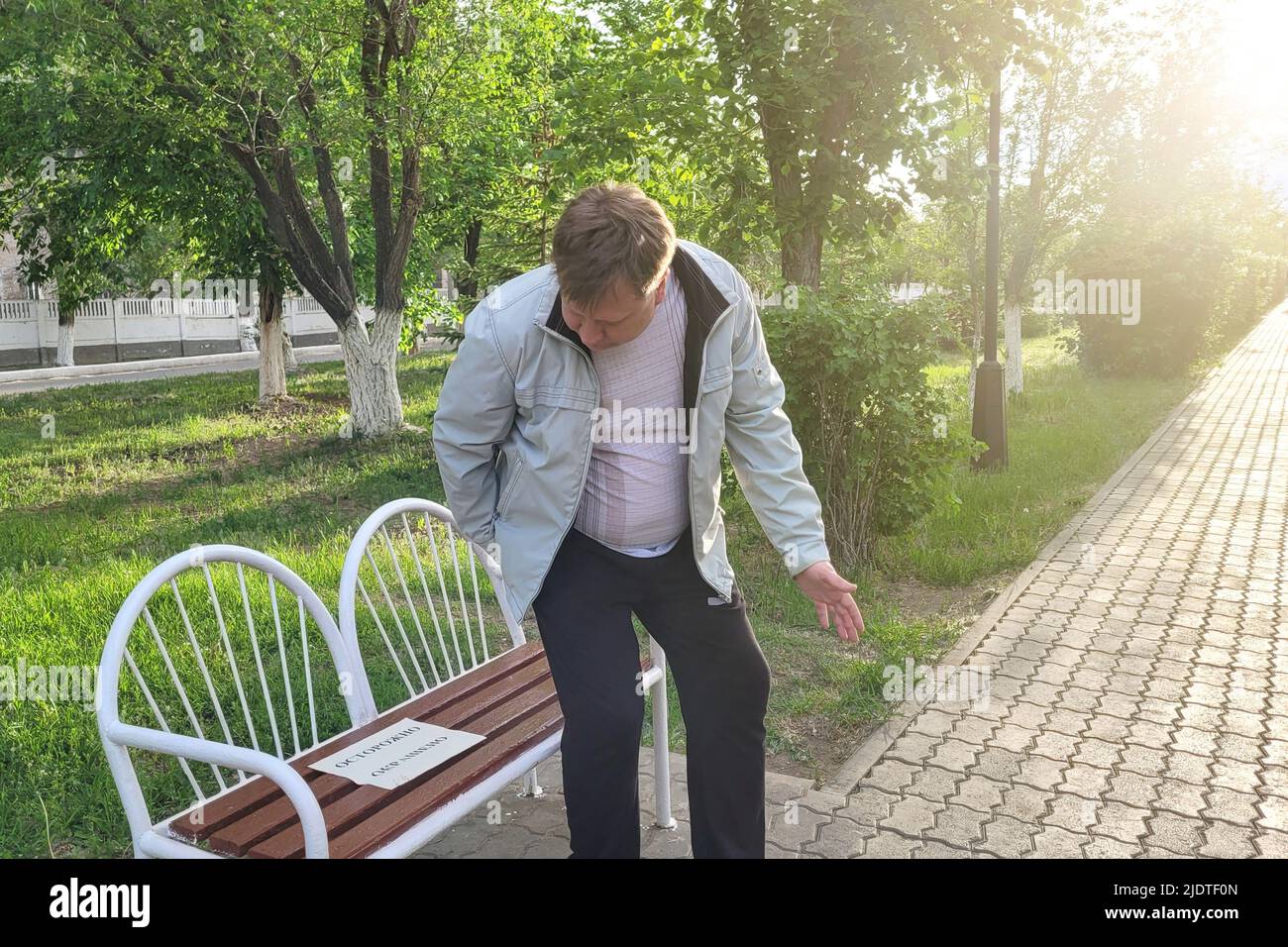 An adult man soiled his clothes and hands on a painted bench in the park. The inscription on the paper is carefully colored. Stock Photo