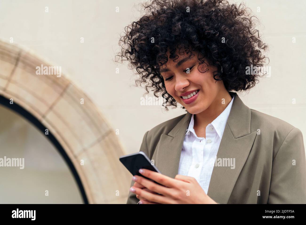 portrait of a young woman with curly hair smiling happy typing a message with her mobile phone, concept of youth and technology, copy space for text Stock Photo