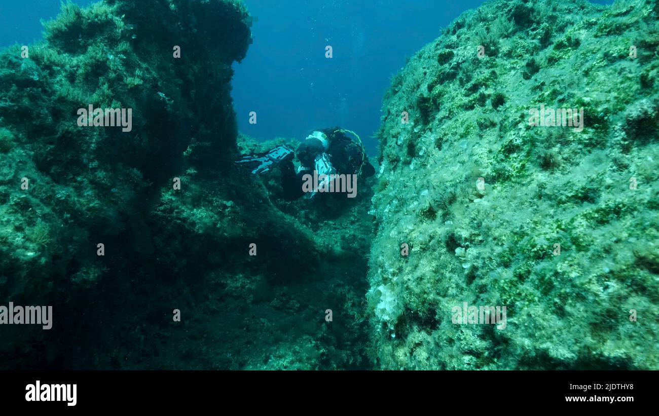 Scuba diver swim through a crack in the rock. Crack in the seabed over tectonic plates. Tiktanic displacement of plates at the bottom of sea. Mediterr Stock Photo