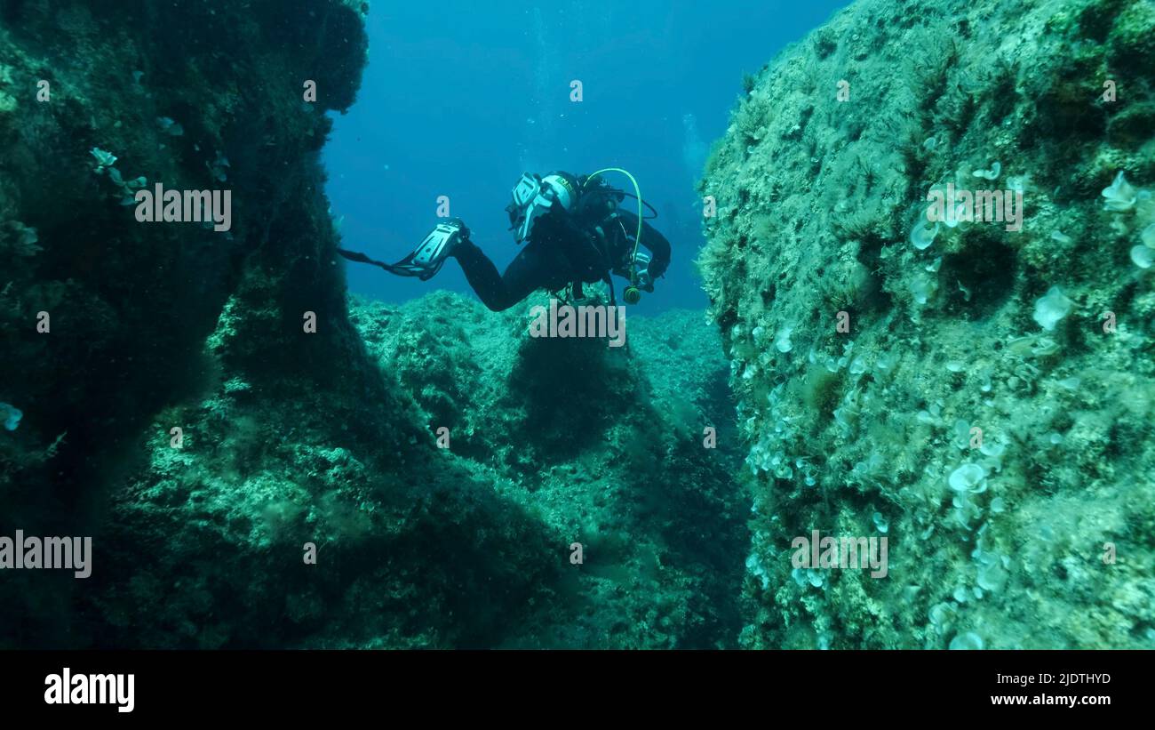 Scuba diver swim through a crack in the rock. Crack in the seabed over tectonic plates. Tiktanic displacement of plates at the bottom of sea. Mediterr Stock Photo