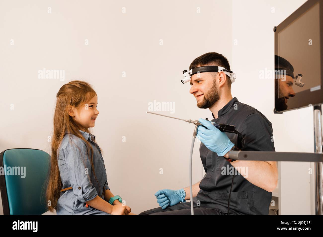 ENT doctor otolaryngologist with headlight showing to child endoscope