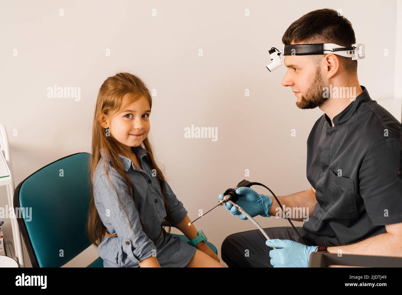 ENT doctor otolaryngologist with headlight showing to child endoscope