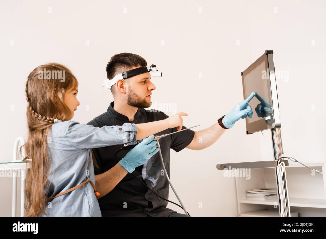 ENT doctor otolaryngologist with headlight showing to child endoscope