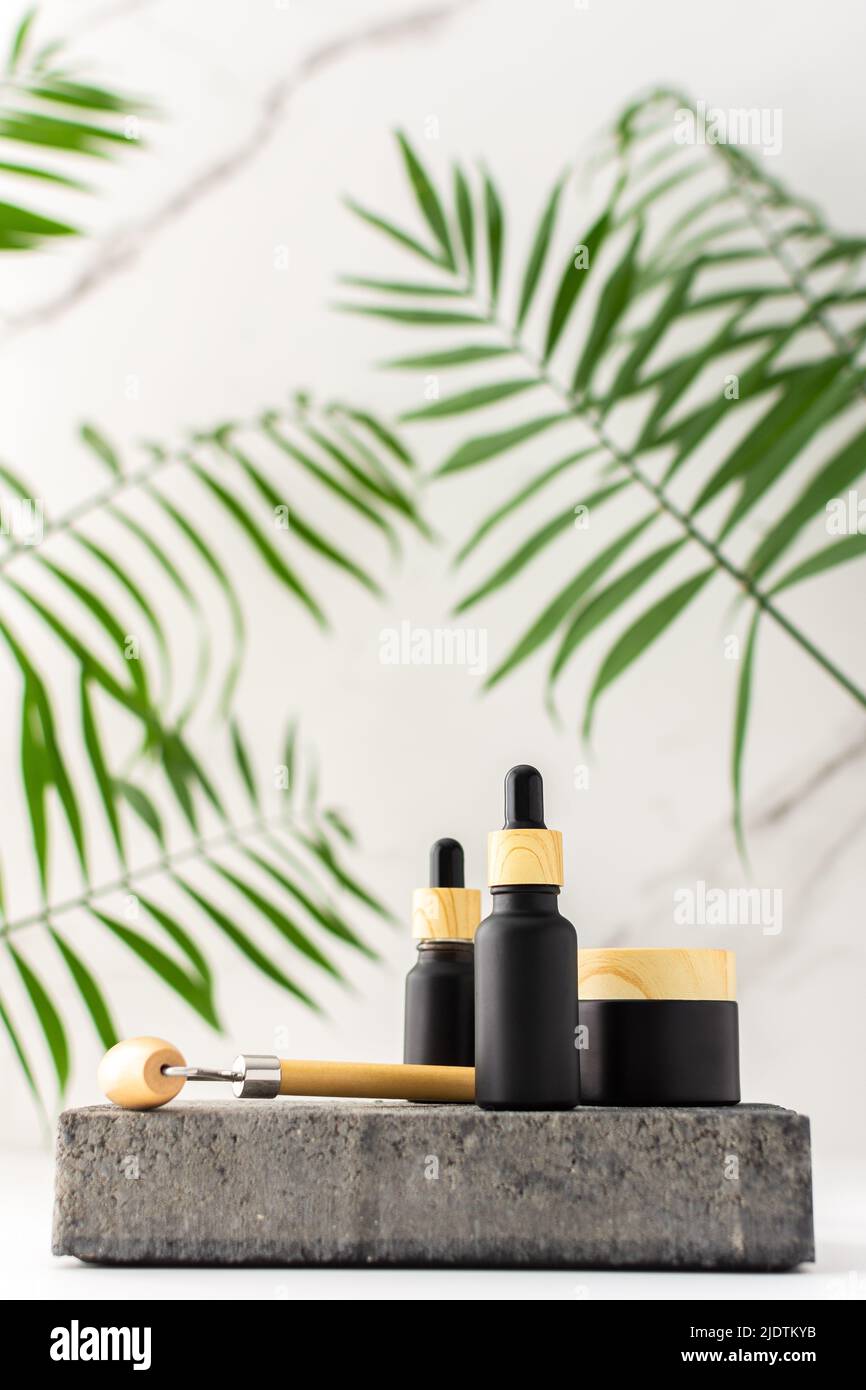 Concrete black podium for cosmetic products close-up among tropical leaves against the background of a marble white wall, bottle with a pipette Stock Photo