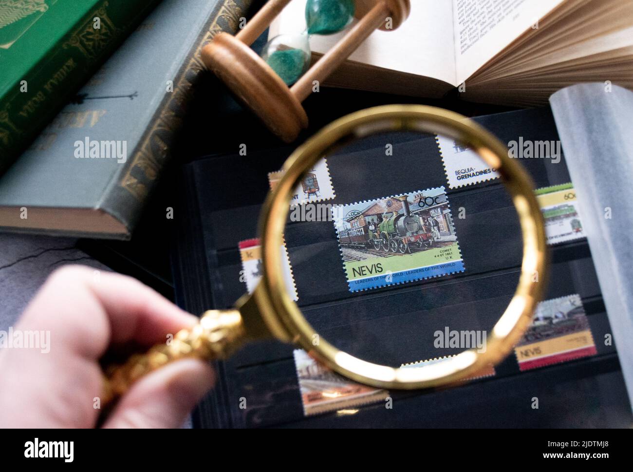 Moscow, Russia, March 2022: Hobby - stamp collecting. Looking at an 60 cent stamp of Nevis with locomotiv through a golden magnifying glass. Old books Stock Photo