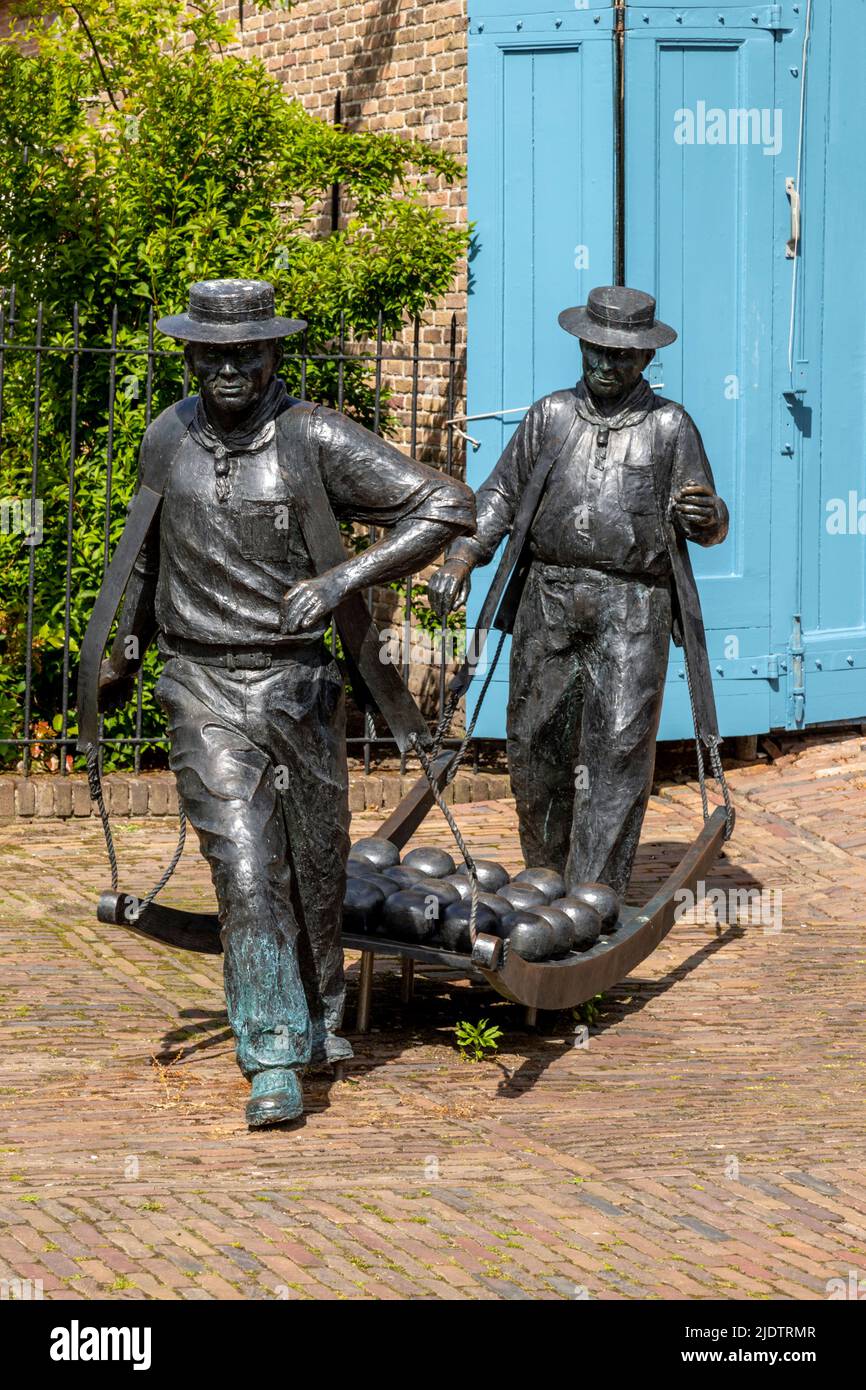 Sculpture of traditional cheese carriers with a load of Edam cheeses on a wooden “berrie” in the market square of Edam, North Holland, The Netherlands Stock Photo