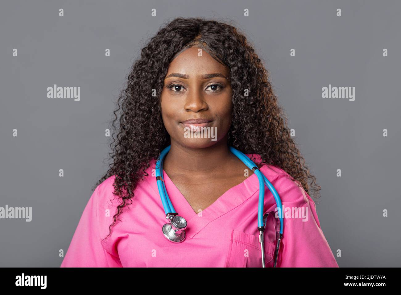 Young doctor black african woman smiling with stethoscope in pink uniform on gray background. Stock Photo