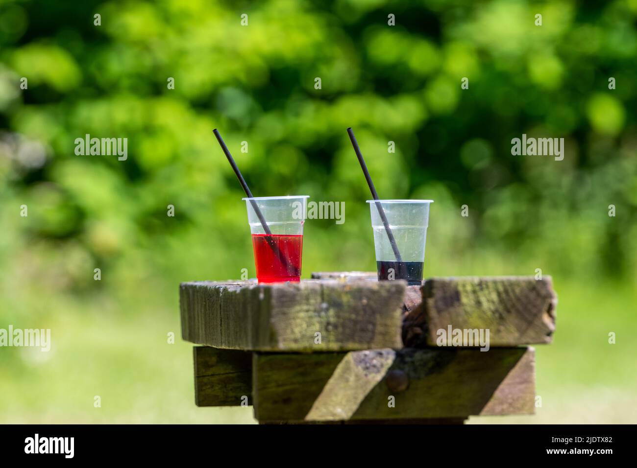 Two plastic drinks glasses, cups or beakers with straws left on a bench