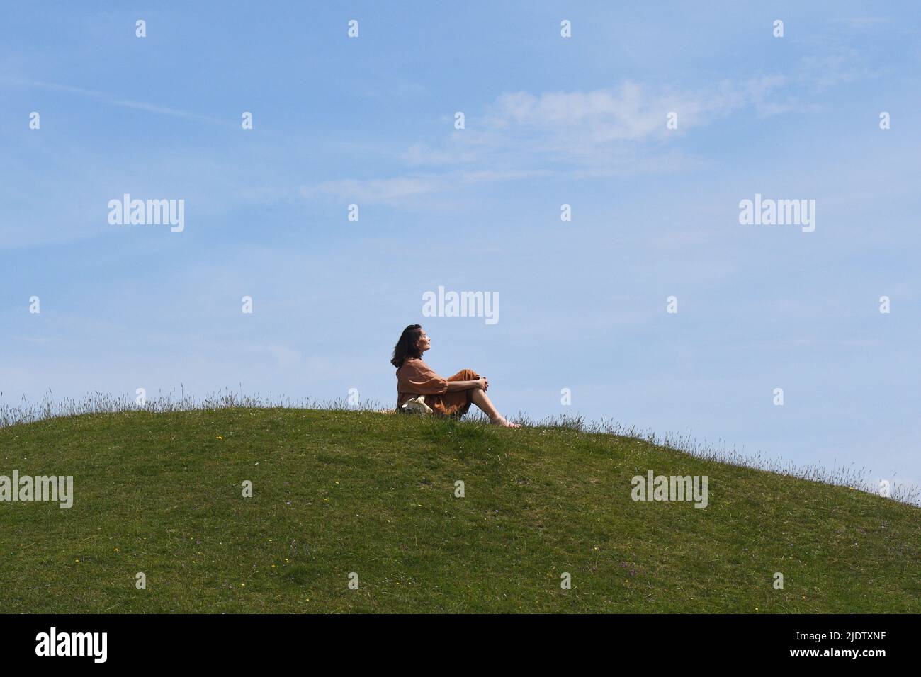 A lady enjoying the mid-summer sun on a green hilltop in Wiltshire. Stock Photo