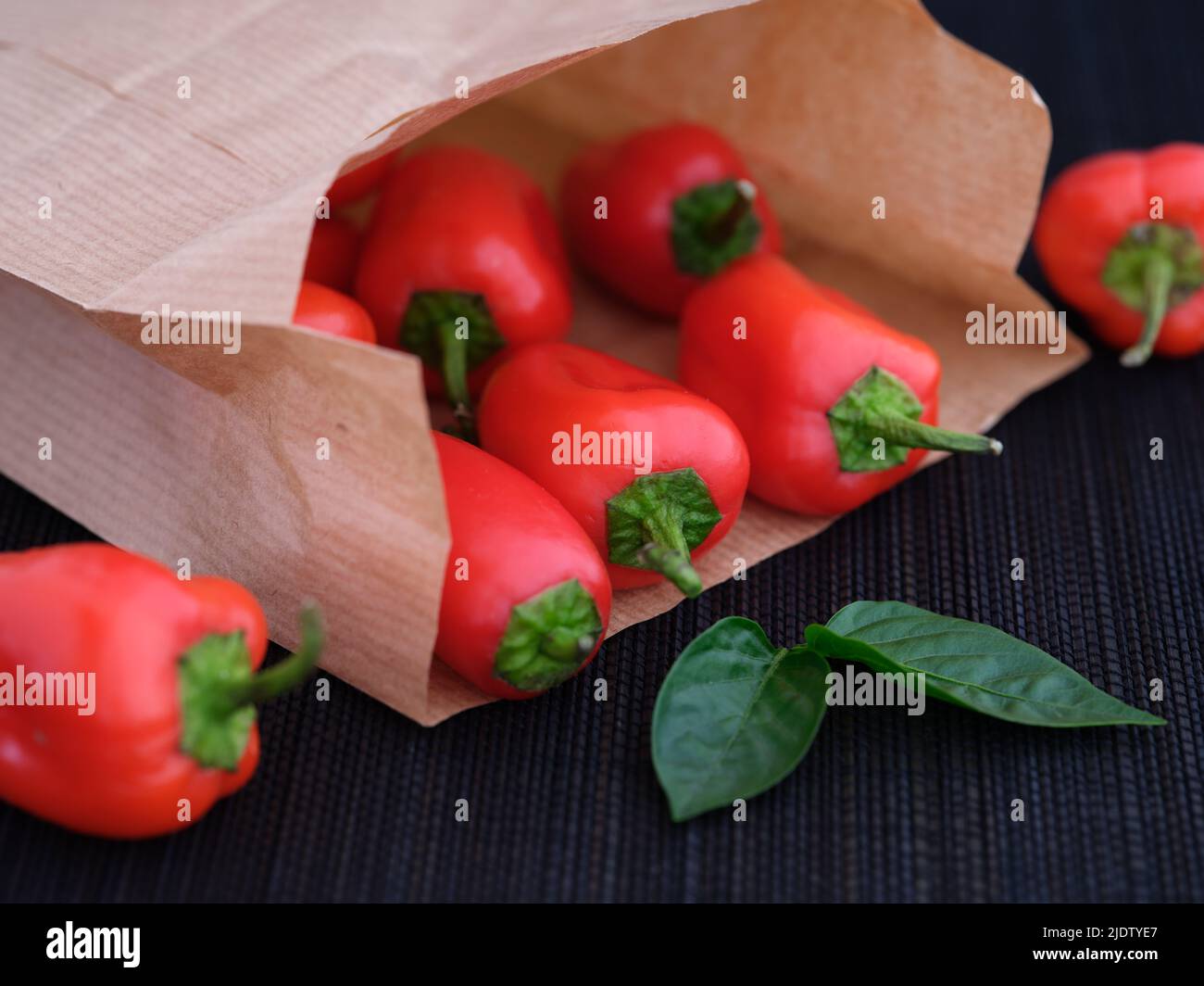 Some red bell peppers lying in a paper bag with some leaves near it. Shallow depth of field. Close up. Stock Photo