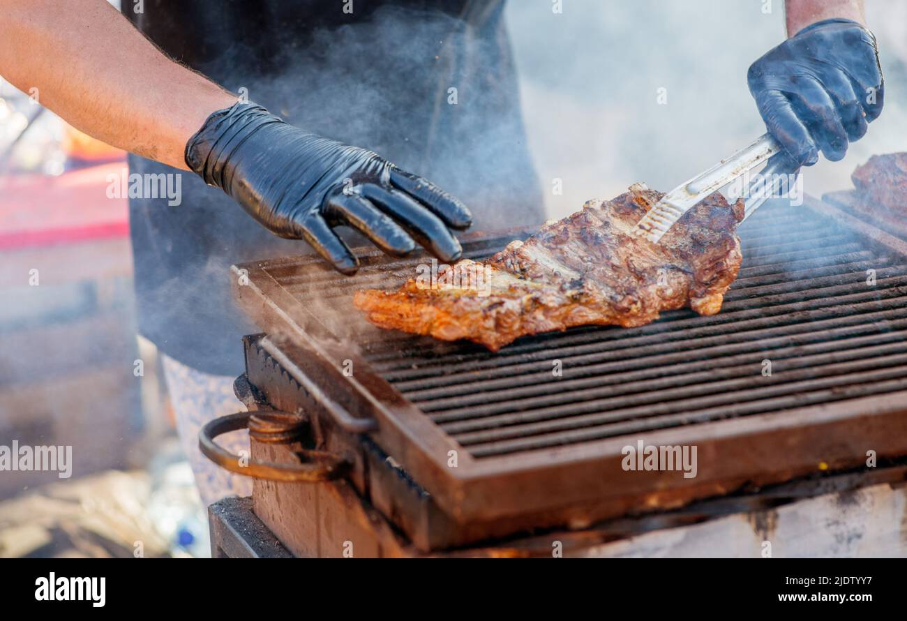 Barbecue ribs. Man in gloves flips grilled ribs on a charcoal grill