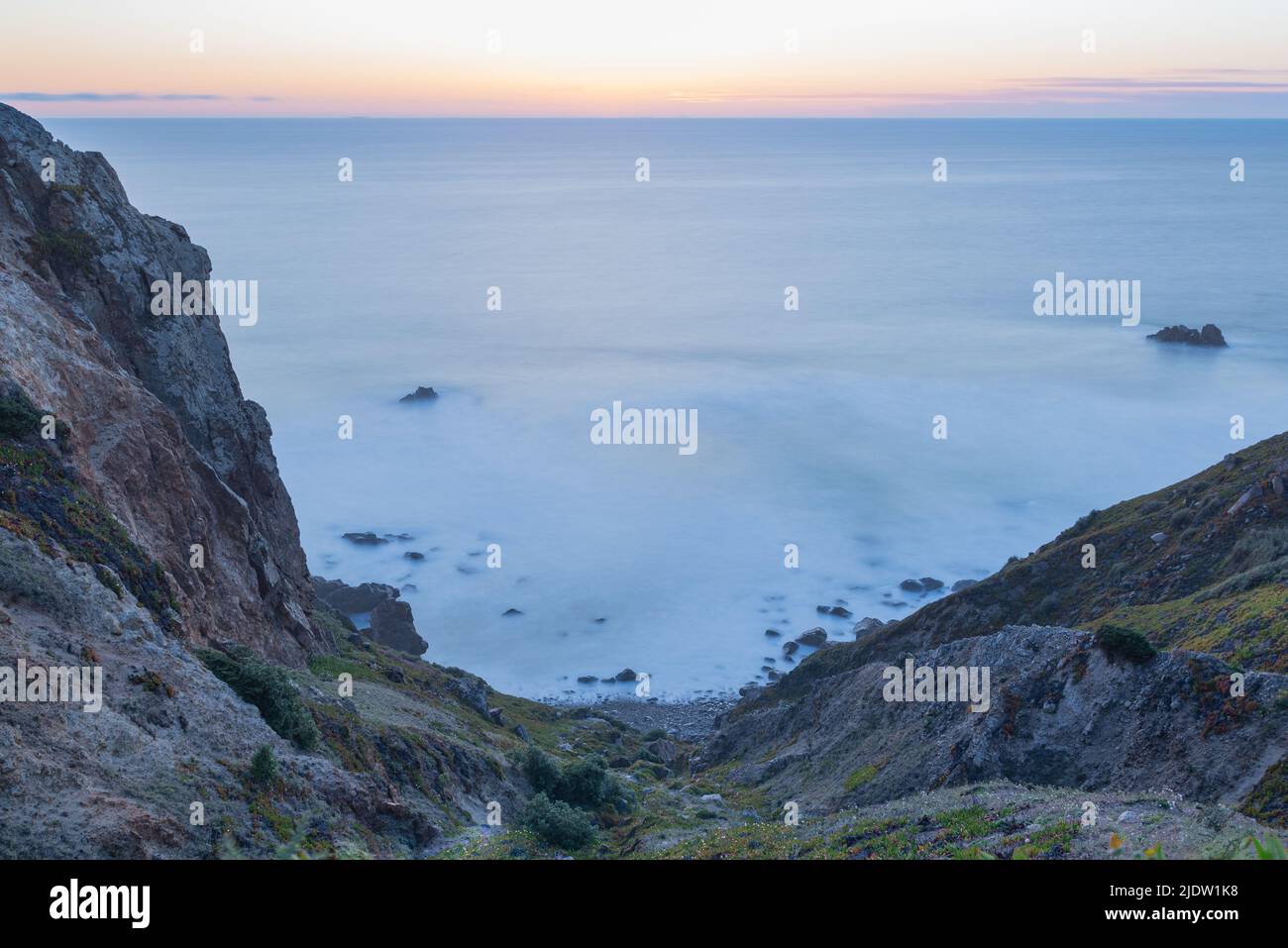 Blurred waves in twilight blue hour sunset long exposure photo of rocky slope leading down to Atlantic Ocean in Sintra-Cascais Natural Park in Portuga Stock Photo