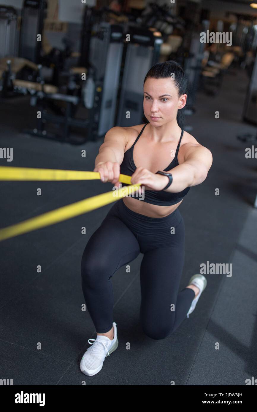 Young woman doing exercise with yellow rubber band in gym Stock Photo