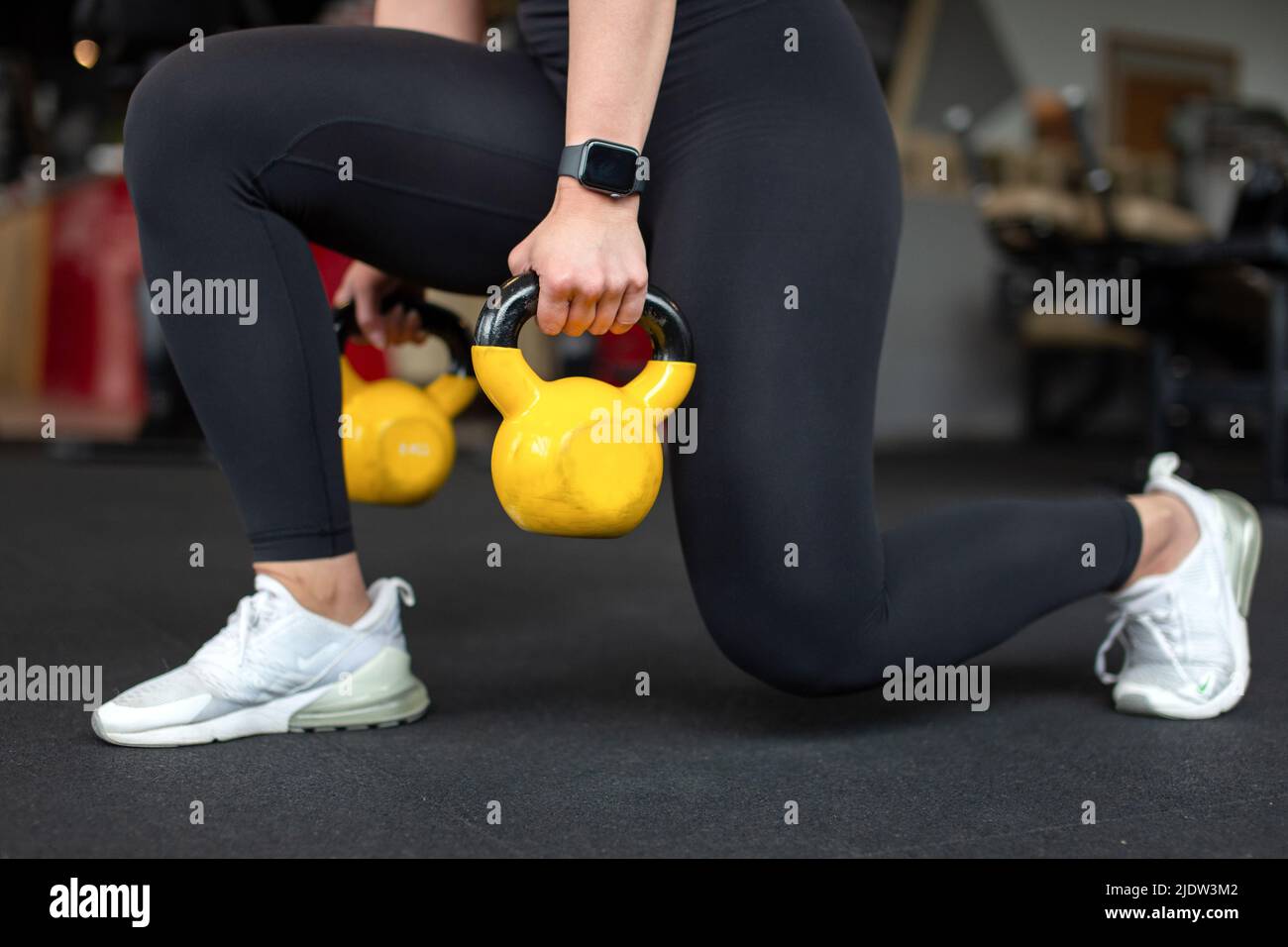 Woman doing lunges in gym by two yellow kettlebell closeup Stock Photo