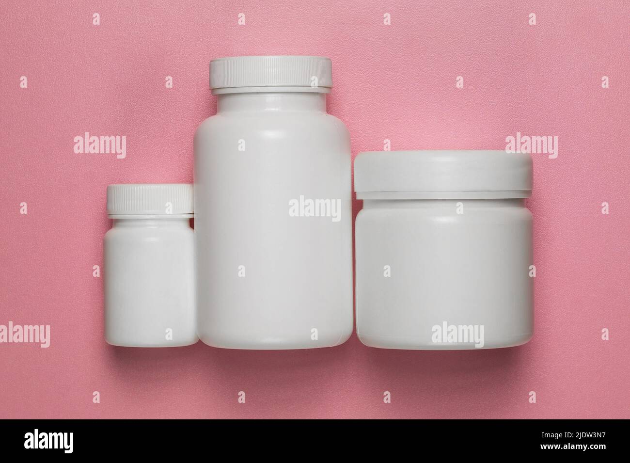 Three empty plastic jars with lids on a pink background Stock Photo