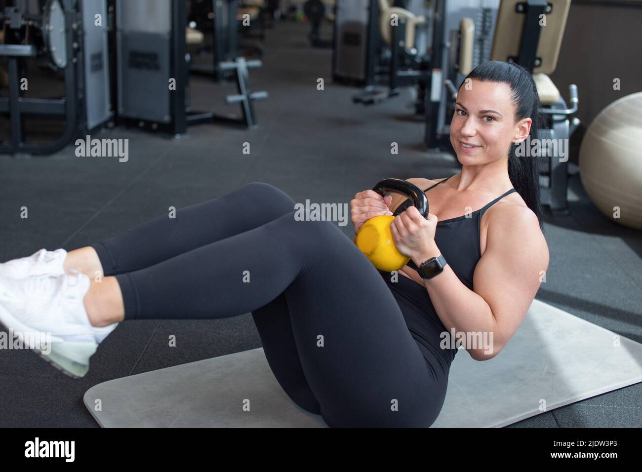 Young woman doing abs workout by kettlebell on floor in gym Stock Photo